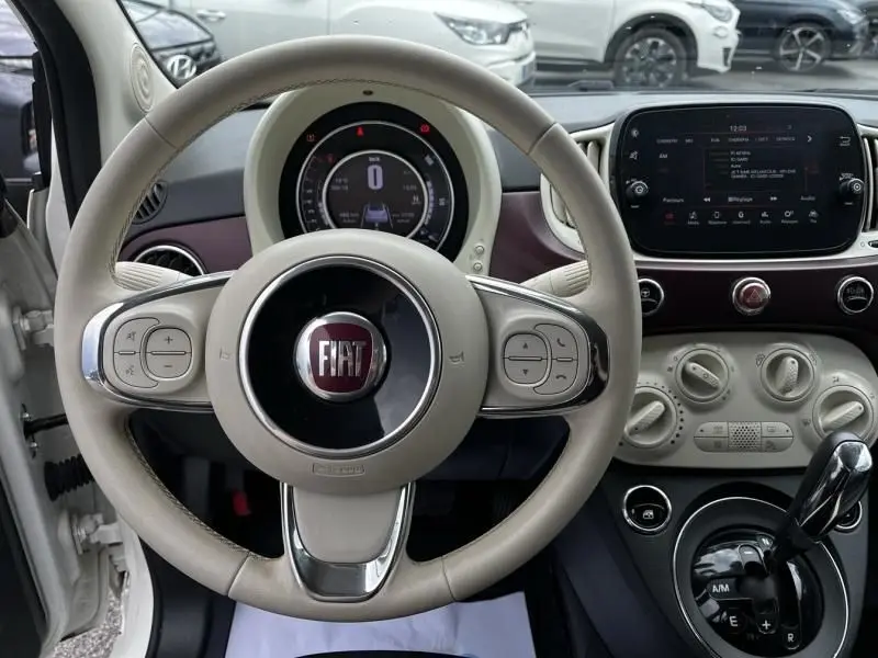 Vue intérieure centrée sur le volant beige de la Fiat 500C blanche 2020, avec tableau de bord numérique et console centrale visible.