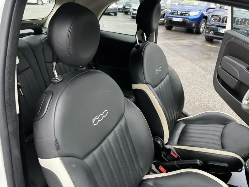 Vue intérieure sur les sièges avant noirs avec logo 500, dans une Fiat 500C blanche, porte ouverte côté droit.