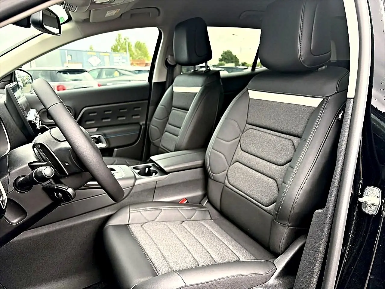 Vue intérieure côté conducteur du Citroën C5 Aircross noir 2025, sièges en cuir et tissu avec accoudoir central.