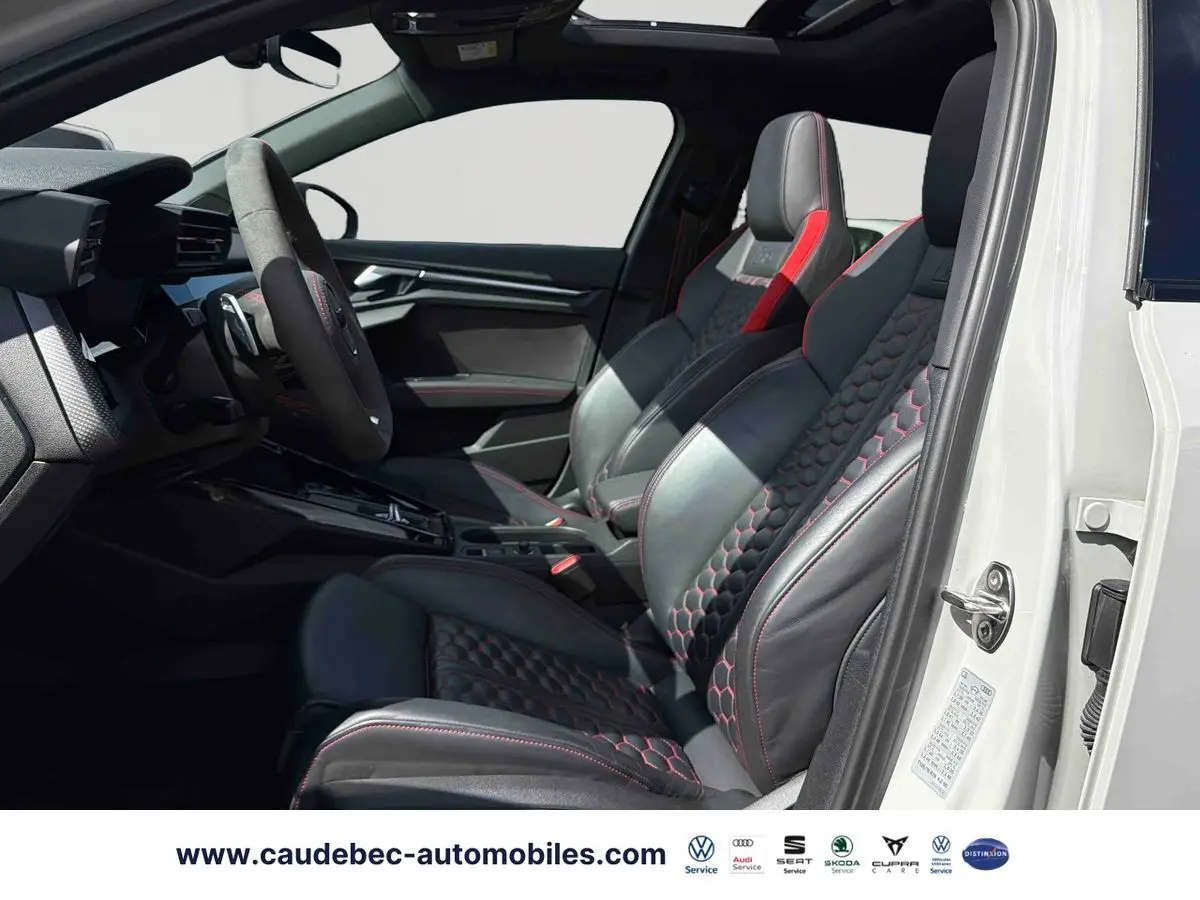 Vue intérieure côté gauche de l'Audi RS3 Sportback avec sièges sport en cuir noir à surpiqûres rouges et toit panoramique ouvert.