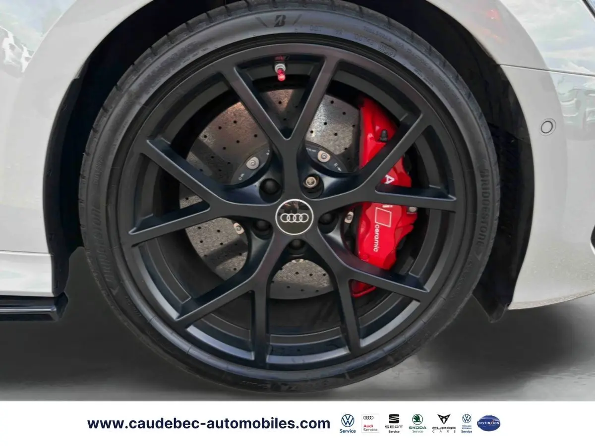 Gros plan sur la jante noire mat à 5 branches en Y de l'Audi RS3 Sportback grise avec étrier de frein céramique rouge visible.