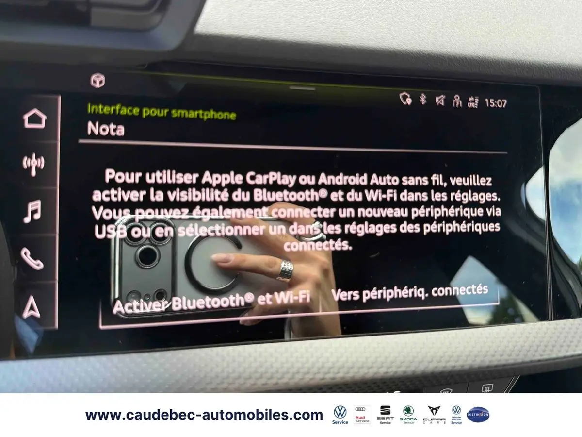 Écran tactile intérieur affichant l'interface smartphone d'une Audi RS3 Sportback grise, avec reflet de main au volant.