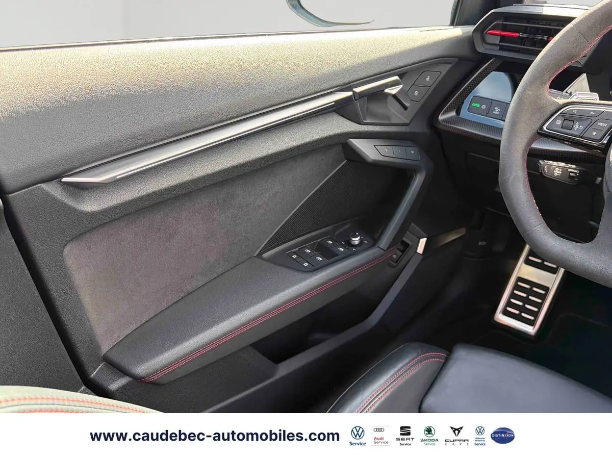 Vue intérieure côté conducteur de l'Audi RS3 Sportback 2022, avec garniture noire et surpiqûres rouges visibles sur la porte et le volant.
