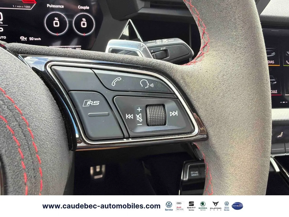 Gros plan sur le volant en cuir avec surpiqûres rouges et commandes RS d'une Audi RS3 Sportback grise, intérieur moderne.