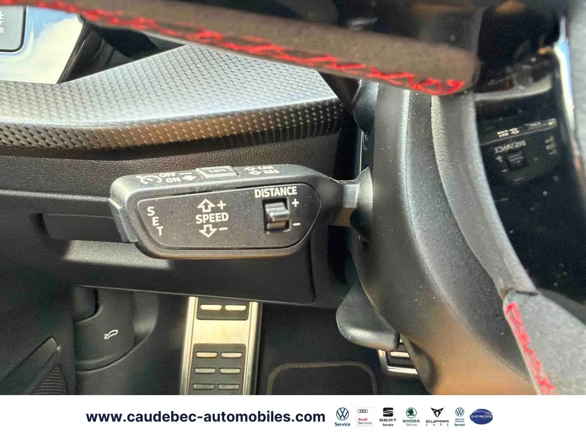 Gros plan sur la commande de régulateur de vitesse au volant d’une Audi RS3 Sportback grise avec surpiqûres rouges.