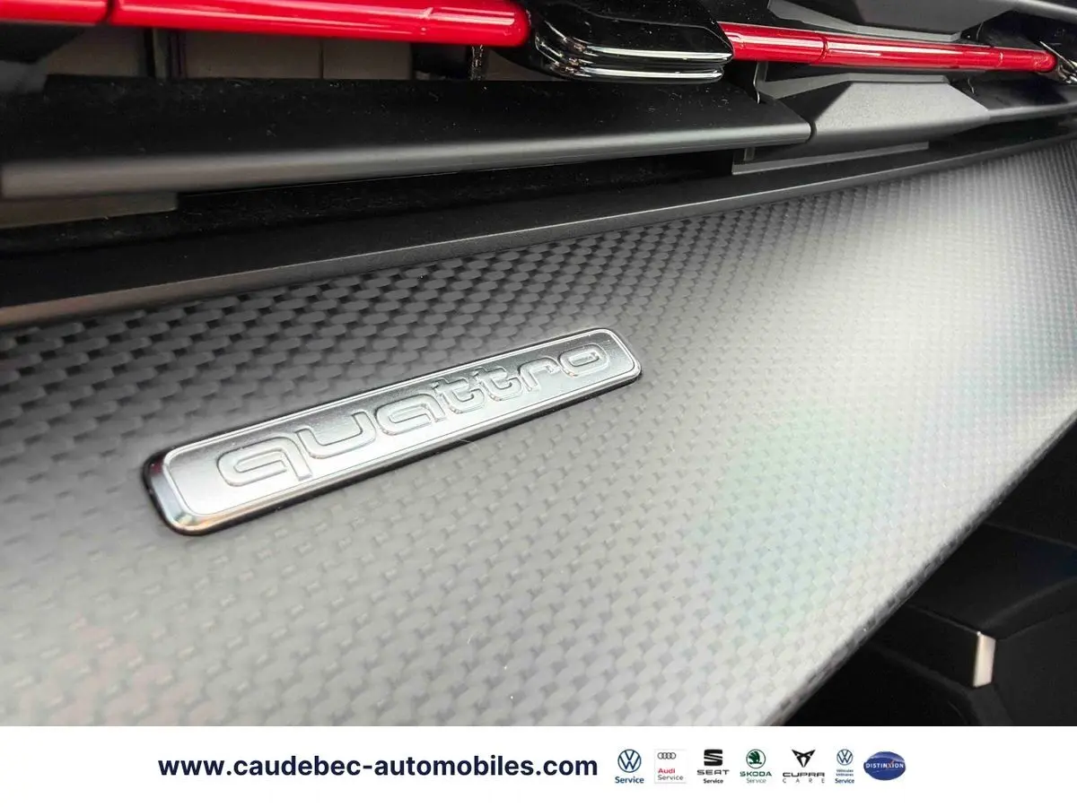 Détail intérieur du tableau de bord en carbone avec logo Quattro argenté et éléments rouges sur Audi RS3 Sportback.