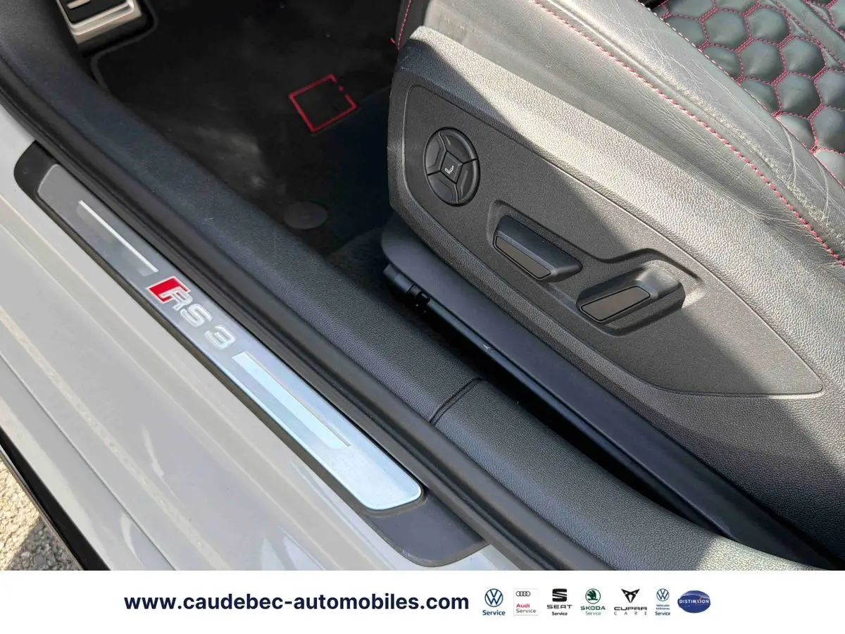 Gros plan sur la plaque de seuil RS3 et le siège en cuir noir avec surpiqûres rouges d'une Audi RS3 Sportback grise.