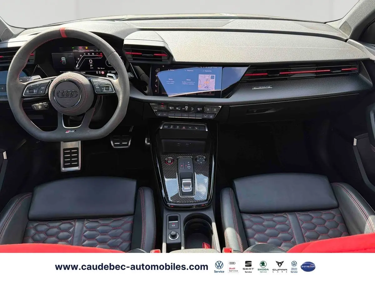 Vue intérieure avant de l’Audi RS3 Sportback 2022 avec volant sport, surpiqûres rouges et inserts carbone sur la console centrale.