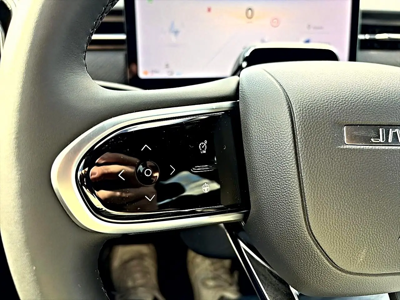 Gros plan sur les commandes multifonctions à gauche du volant gris du JAECOO J7, avec écran tactile en arrière-plan.