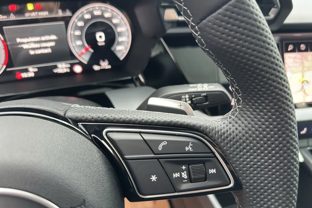 Gros plan sur le volant cuir perforé avec palettes et commandes audio de l'Audi A3 TFSI 150 Hybrid S-Line 2025.