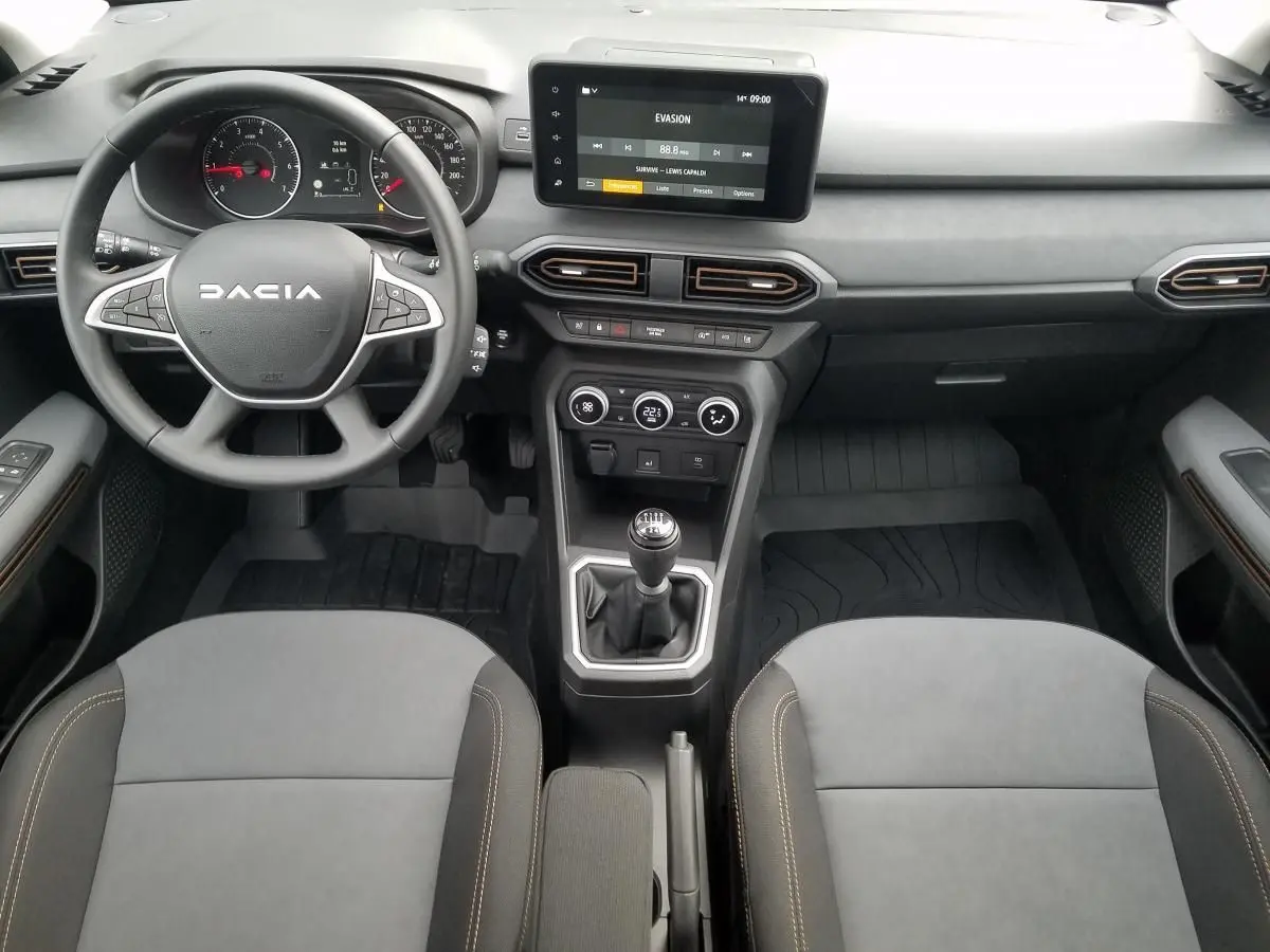Vue intérieure frontale du tableau de bord et des sièges avant gris du Dacia Jogger 2025 avec boîte manuelle.