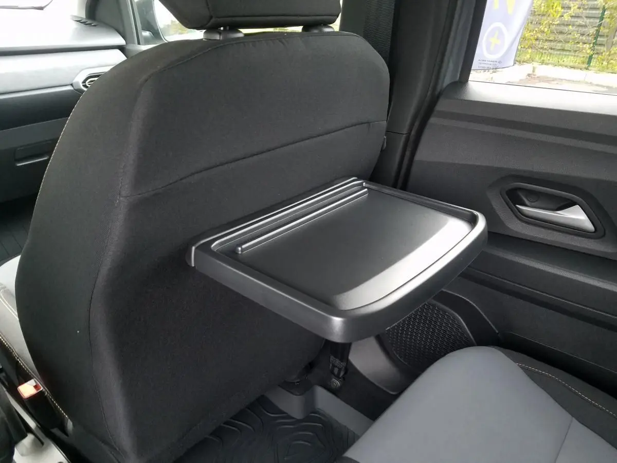 Tablette rabattable noire fixée au dossier du siège avant dans l'habitacle arrière du Dacia Jogger gris urbain.