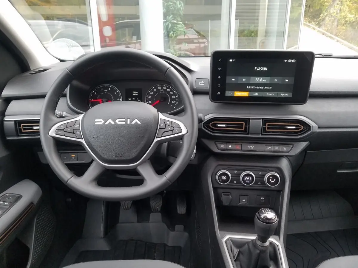 Vue intérieure du tableau de bord du Dacia Jogger gris urbain 2025, volant multifonction et écran tactile central.
