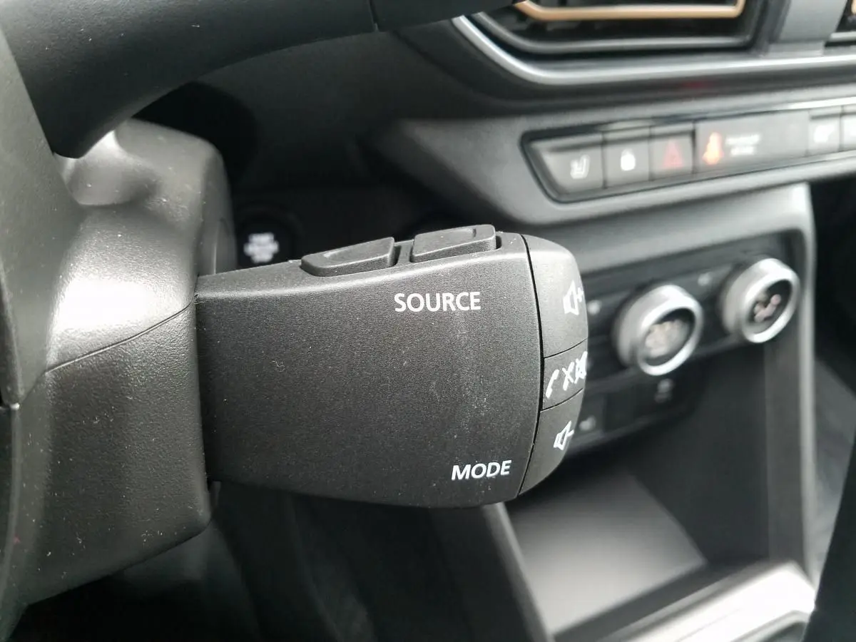 Gros plan sur la commande au volant de la DACIA JOGGER 2025, avec boutons source et mode visibles, intérieur noir.