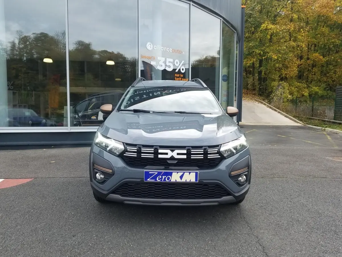 Vue frontale d'un Dacia Jogger gris urbain 2025 avec feux LED allumés et barres de toit visibles.