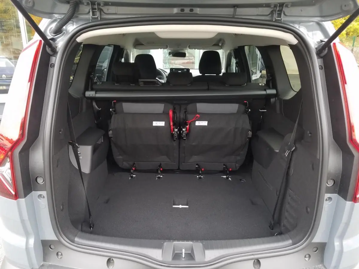 Coffre ouvert d'un Dacia Jogger gris urbain 2025, montrant la troisième rangée de sièges rabattue et l'intérieur spacieux.