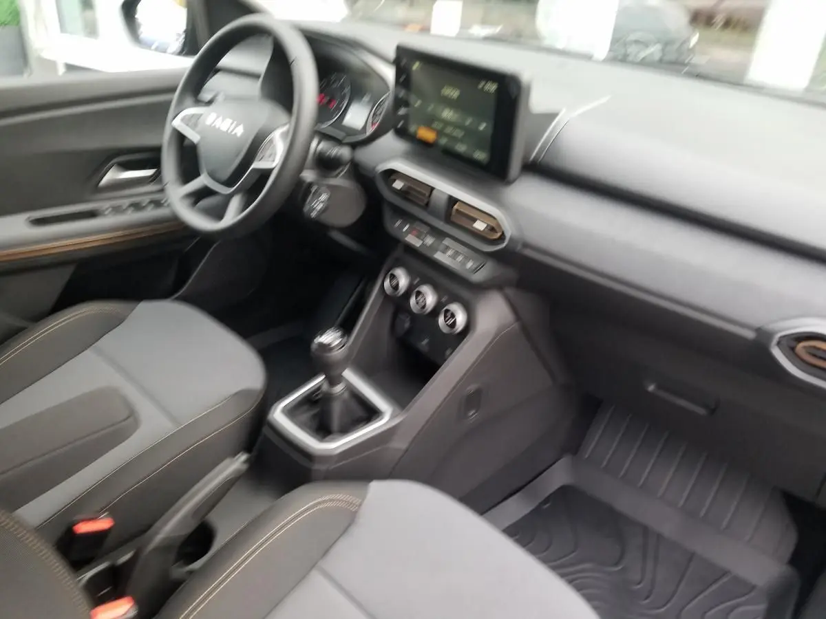 Intérieur du Dacia Jogger 2025 vu côté conducteur, sièges gris avec surpiqûres, tableau de bord et écran tactile central.