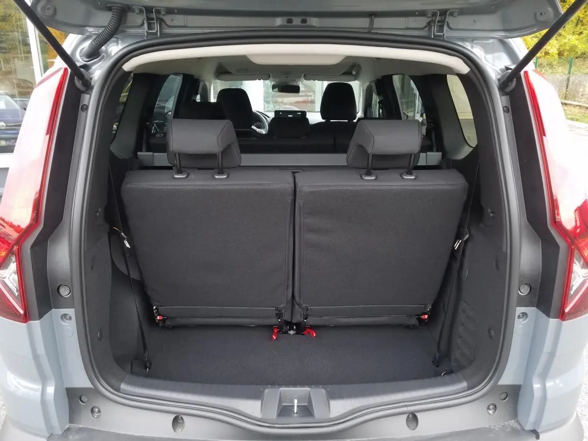 Vue arrière du coffre ouvert d'un Dacia Jogger gris urbain 2025, montrant la troisième rangée de sièges relevée.