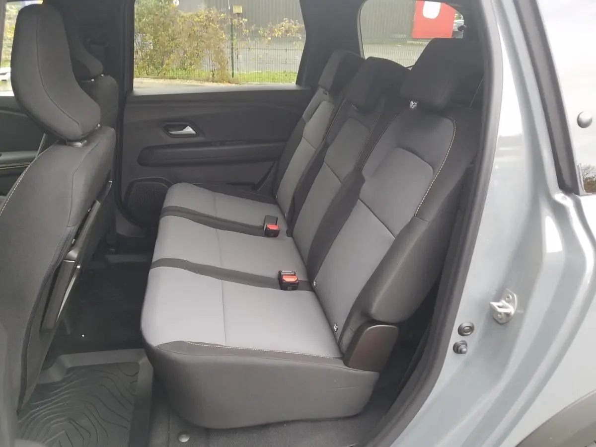 Vue latérale des sièges arrière gris clair et noir du Dacia Jogger 2025 en gris urbain avec porte ouverte côté droit.