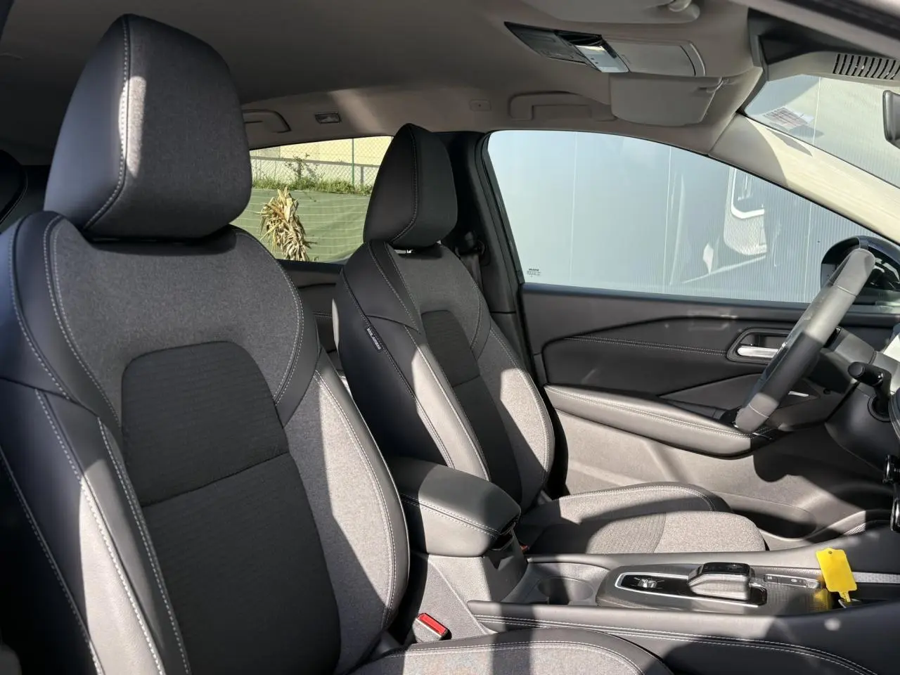Vue intérieure côté droit du Nissan Qashqai III e-Power 2025, sièges avant gris et console centrale avec boîte auto.