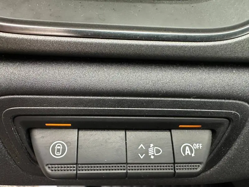 Gros plan sur les commandes intérieures du Renault Captur 2025, boutons de verrouillage, réglage phares et arrêt auto start, tableau de bord noir.