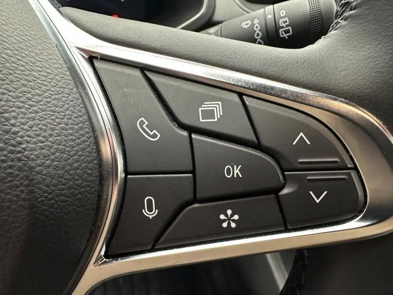 Gros plan sur les commandes multifonctions noires avec cadre chromé du volant côté gauche du Renault Captur 2025 gris/noir.