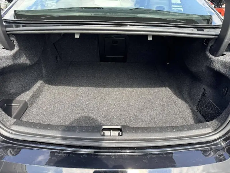 Coffre ouvert vu de l'arrière d'une Volvo S60 2024 gris Brume Métallisé, intérieur spacieux et tapis gris.