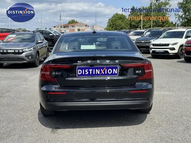 Vue arrière d'une Volvo S60 noire stationnée sur un parking avec plusieurs autres véhicules autour.