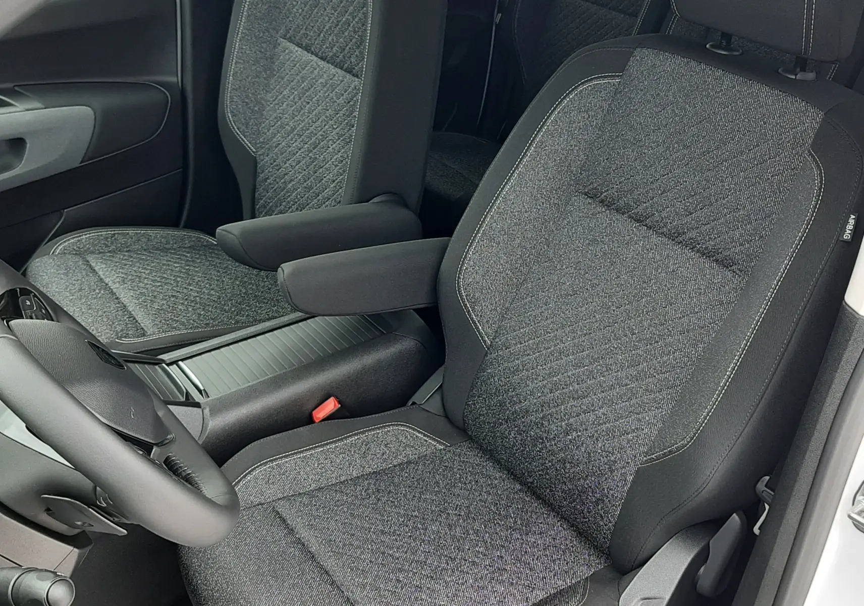Vue intérieure côté conducteur du Peugeot Rifter 2026 blanc Kaolin, sièges tissu gris avec accoudoir central.