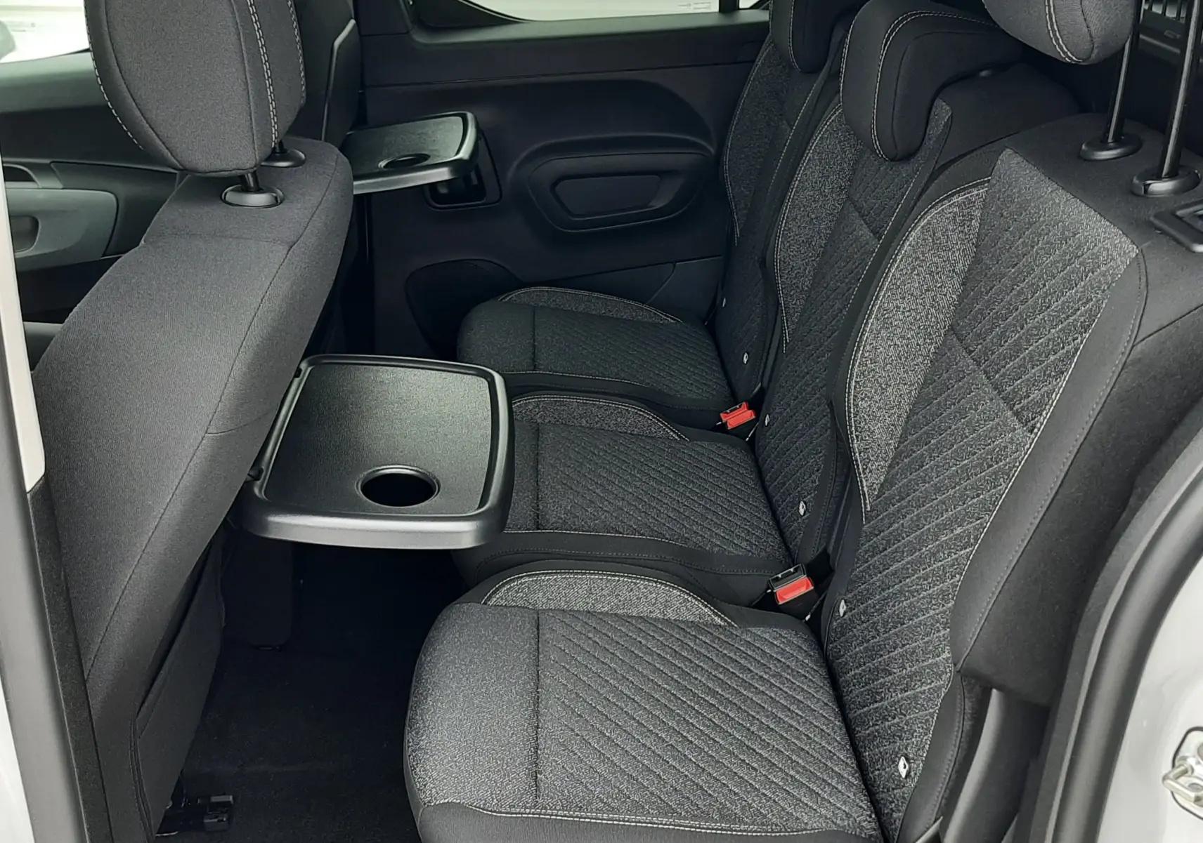 Vue latérale intérieure des sièges arrière gris foncé du Peugeot Rifter blanc Kaolin 2026 avec tablette rabattable.