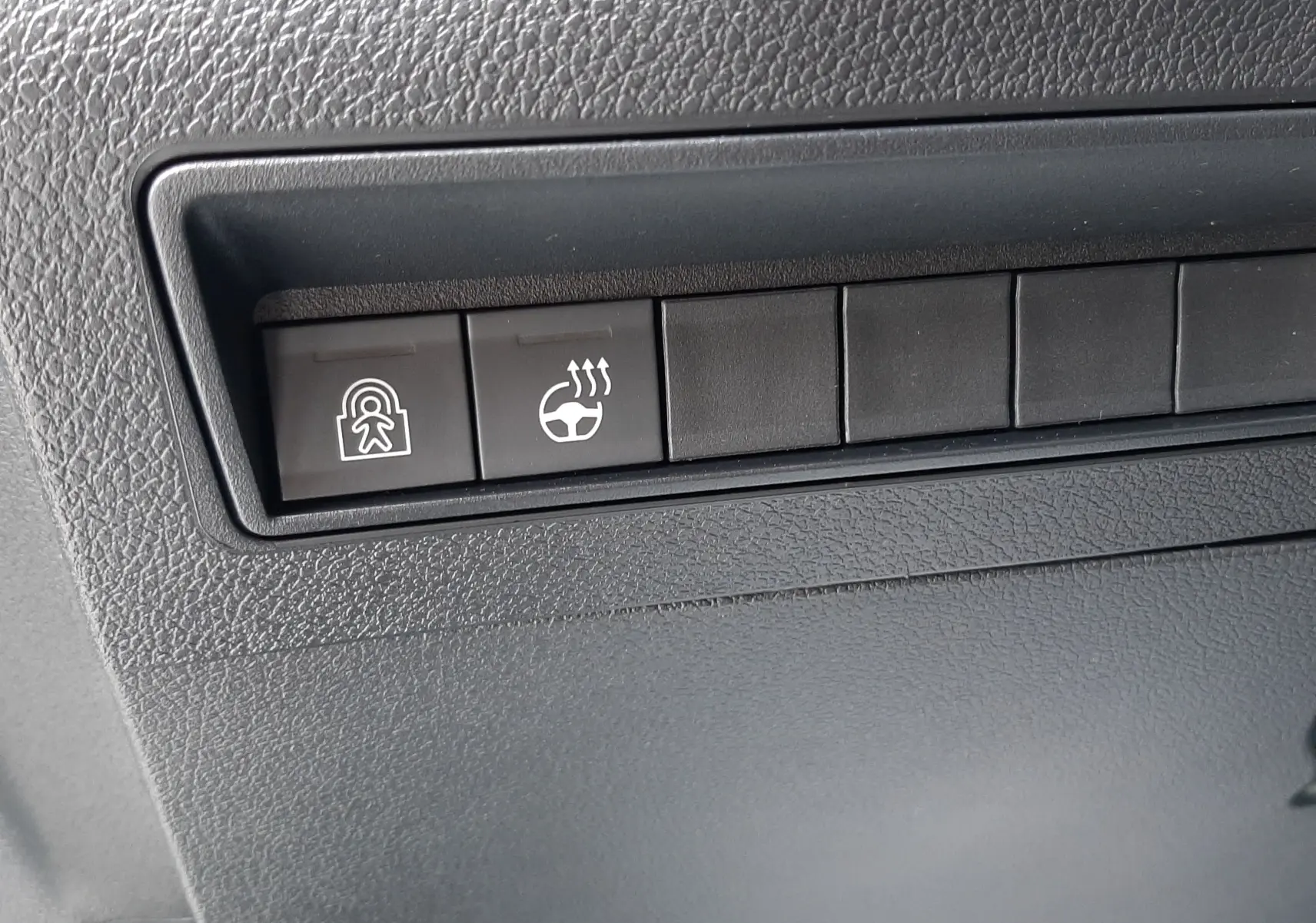 Gros plan sur les boutons de commande du volant chauffant et de sécurité dans l’habitacle gris du Peugeot Rifter blanc Kaolin.