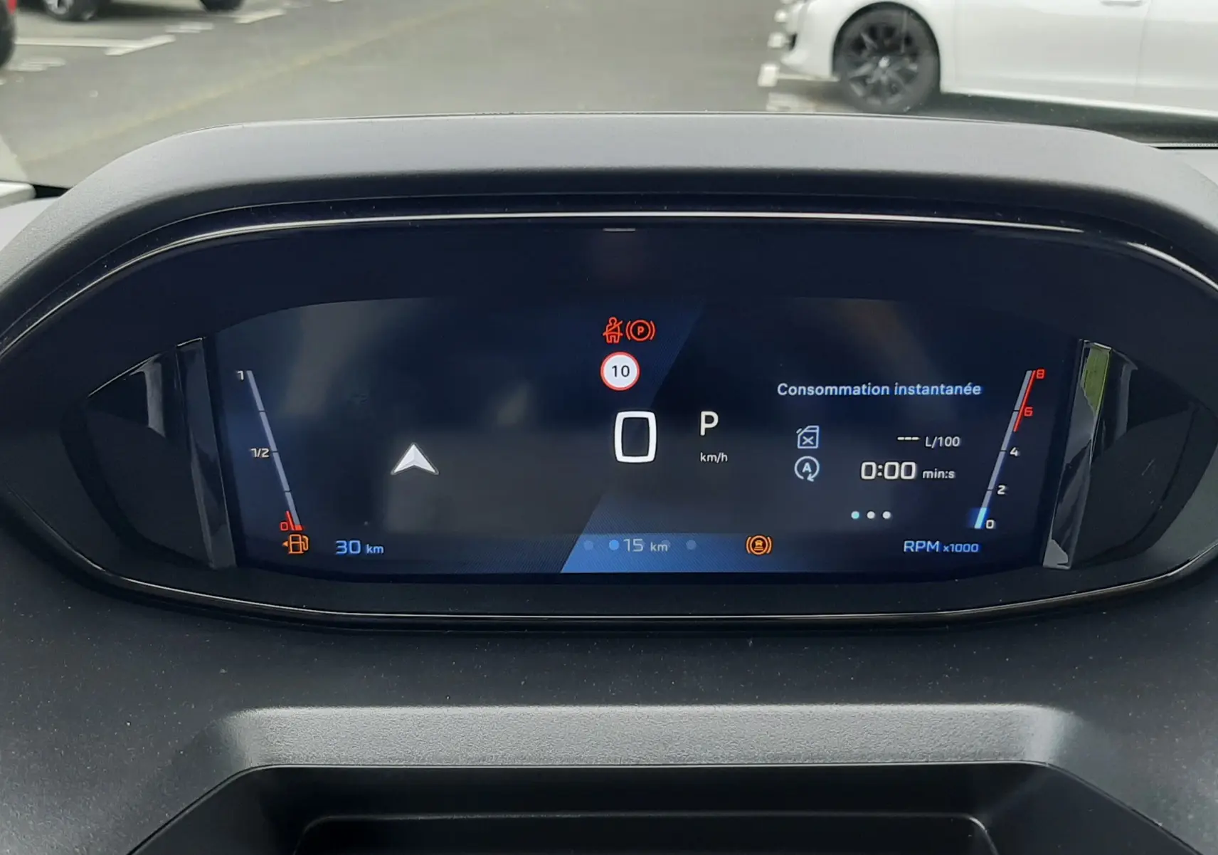 Vue rapprochée du tableau de bord numérique du Peugeot Rifter blanc Kaolin, affichant la consommation instantanée et la vitesse à 0 km/h.