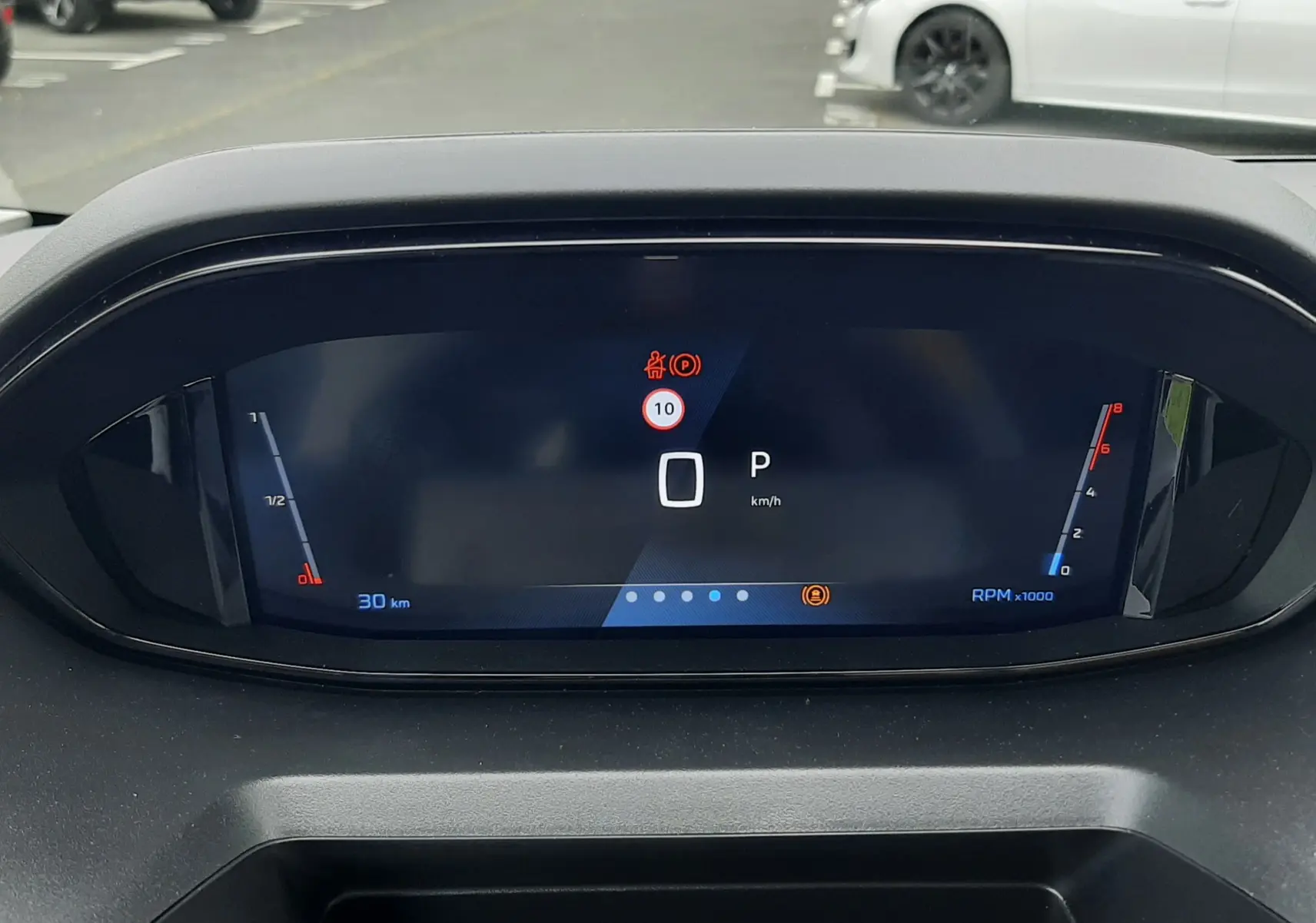 Vue rapprochée du tableau de bord numérique du Peugeot Rifter blanc Kaolin, affichant la vitesse à 0 km/h et le mode parking.