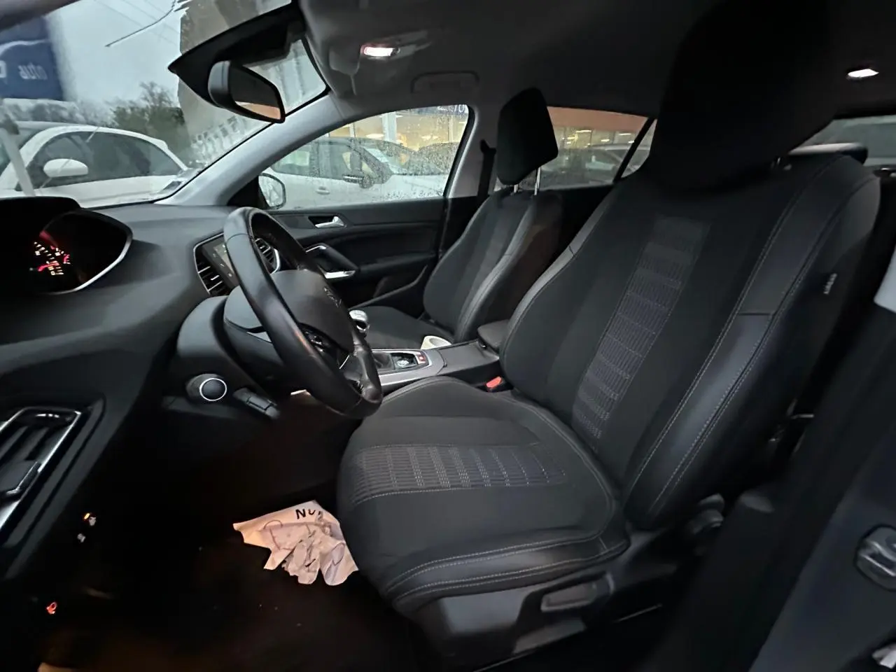 Intérieur avant de la Peugeot 308 gris Artense, vue côté conducteur, sièges tissu noir et tableau de bord visible.