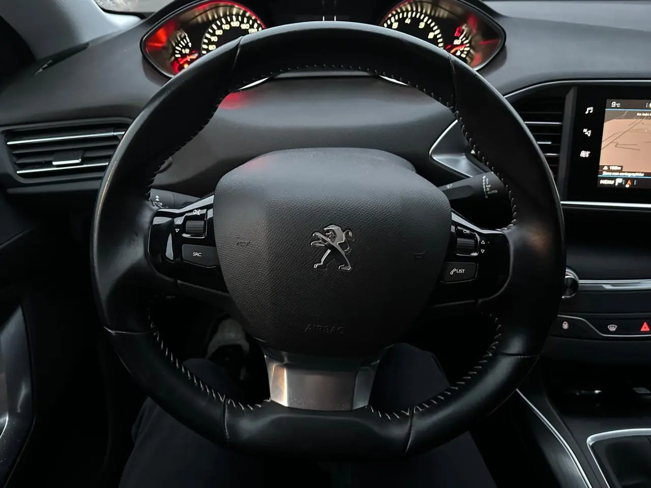 Vue intérieure centrée sur le volant noir de la Peugeot 308 avec tableau de bord et écran tactile visible à droite.