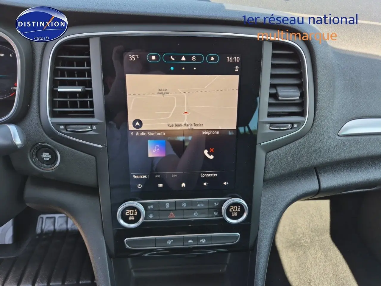 Vue rapprochée du tableau de bord central de la Renault Mégane Break gris titanium avec écran tactile et commandes climatisation.