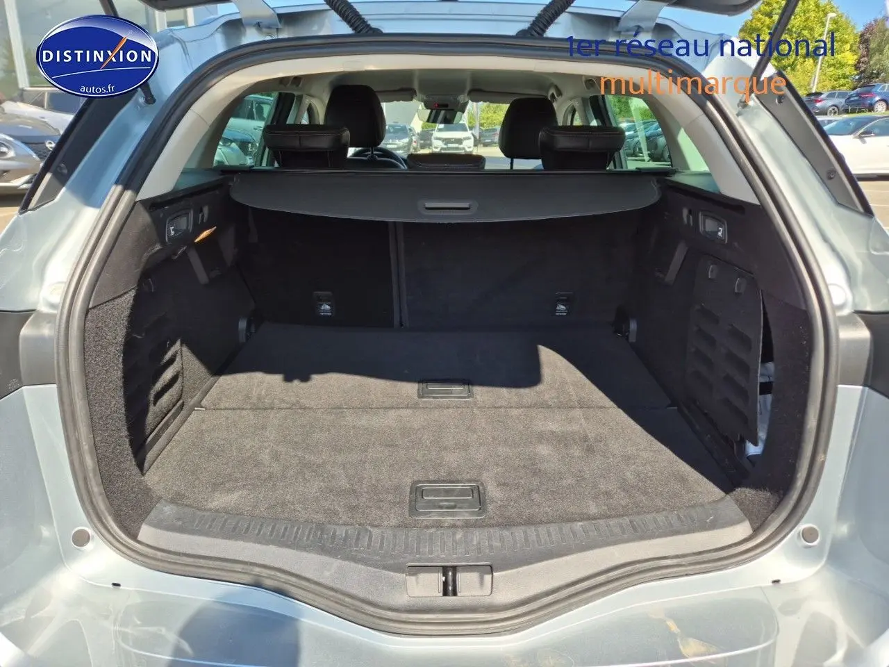 Coffre ouvert vu de l'arrière d'une Renault Mégane Break gris titanium, montrant l'espace de chargement et banquette arrière.