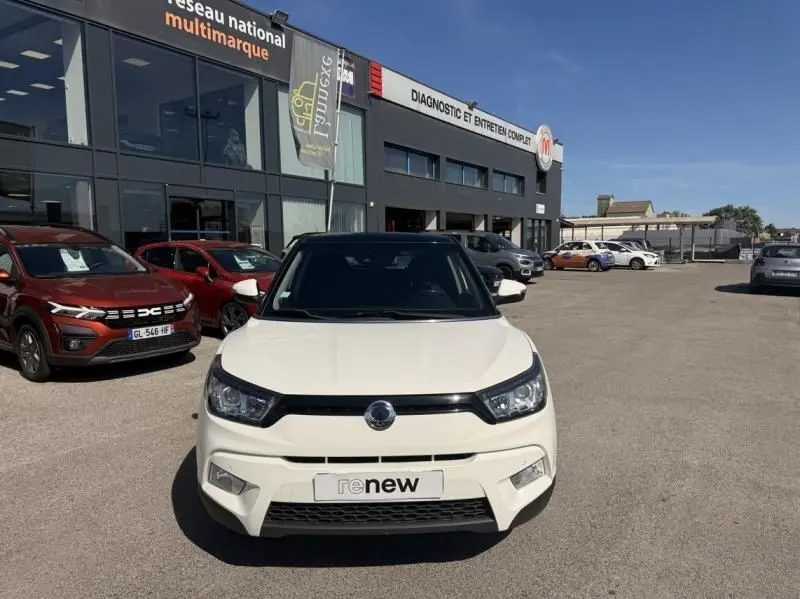 Vue de face d'un SsangYong Tivoli blanc bi-ton avec toit noir, stationné devant un garage multimarque.