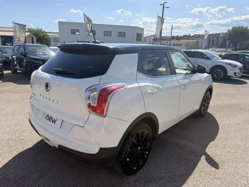 Vue 3/4 arrière droite du SsangYong Tivoli blanc 2017 avec toit noir et jantes noires dans un parking extérieur.