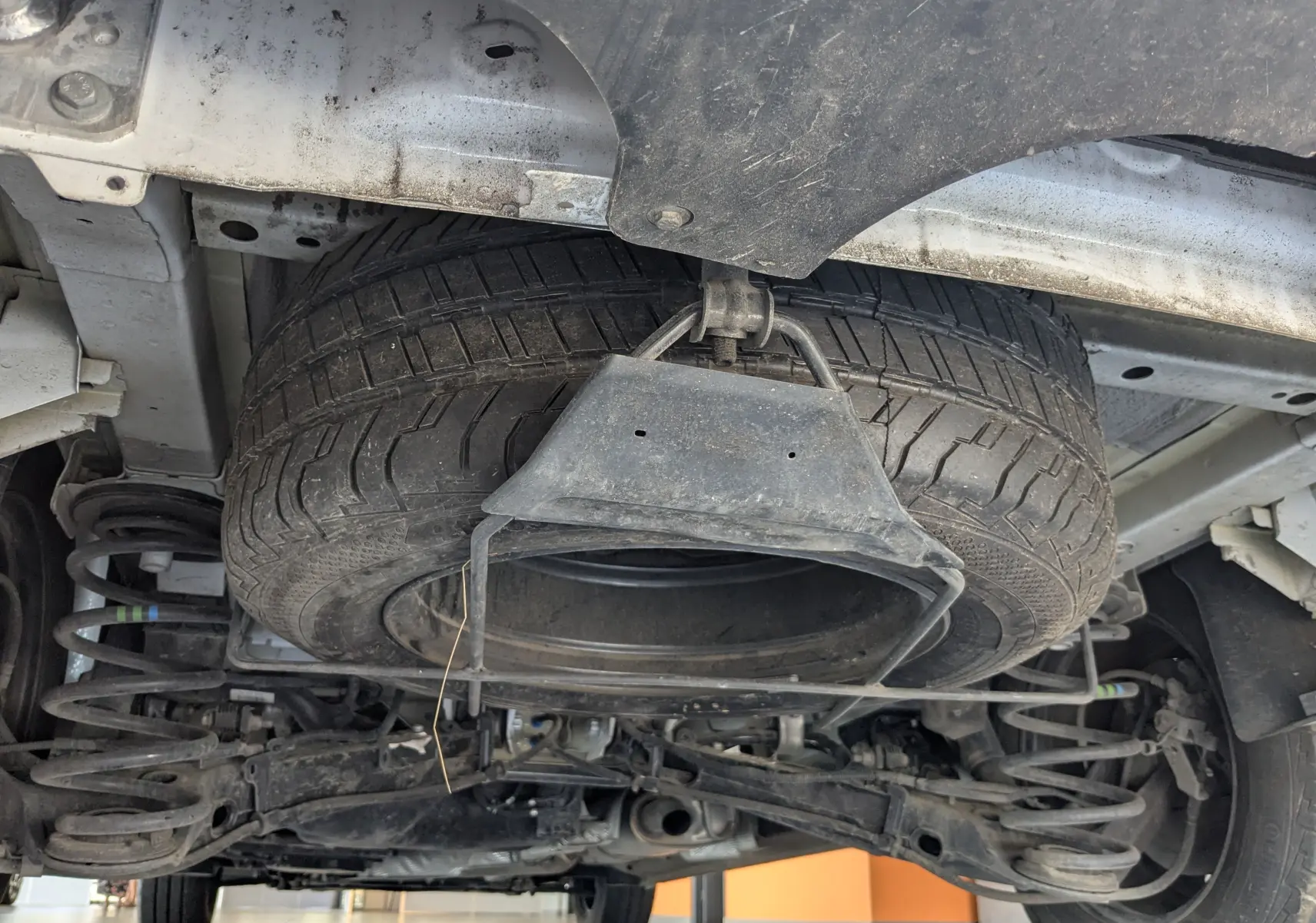 Vue en contre-plongée sous un FIAT Scudo Fourgon blanc 2024, montrant la roue de secours suspendue sous le châssis.