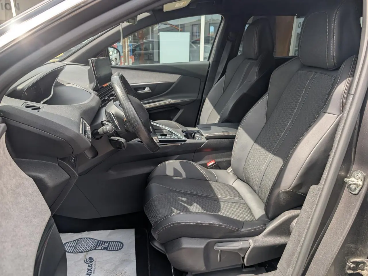 Vue intérieure côté conducteur du Peugeot 5008 gris 2023, mettant en valeur les sièges avant en cuir et le tableau de bord moderne.