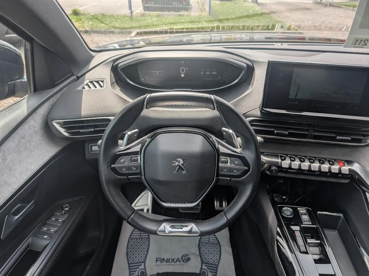 Vue intérieure frontale du volant cuir perforé noir avec badge GT du Peugeot 5008 gris 2023, tableau de bord et écran tactile visibles.