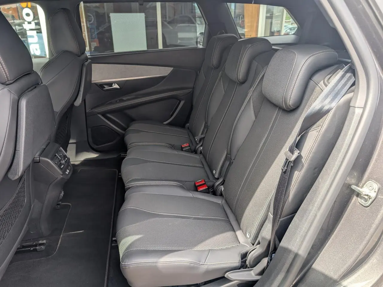 Vue côté droit des trois sièges arrière noirs du Peugeot 5008 2023, avec ceintures et panneaux de porte gris foncé.
