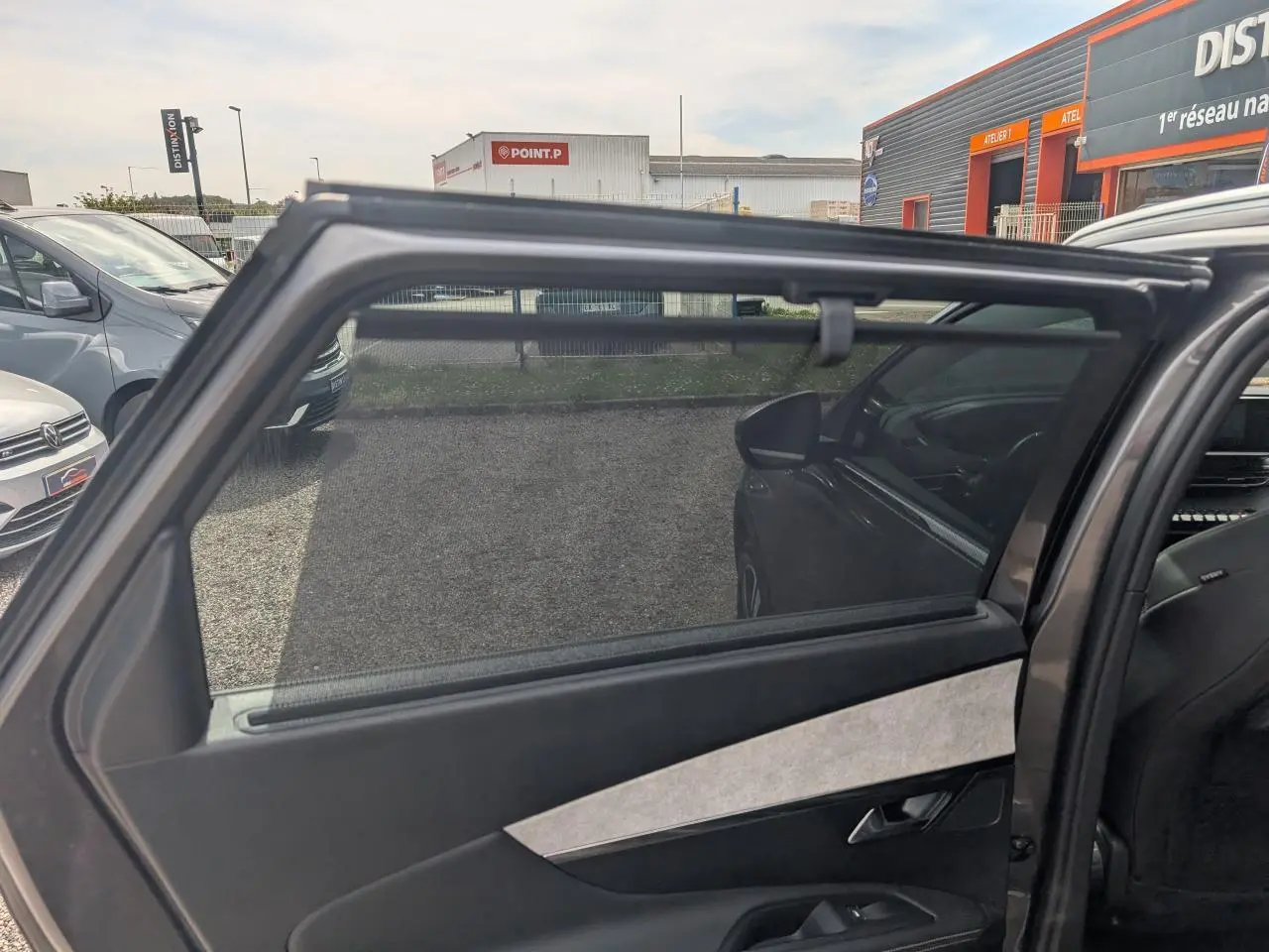 Vue intérieure côté gauche de la porte arrière ouverte d’un Peugeot 5008 gris 2023 avec vitrage surteinté et habillage Alcantara.