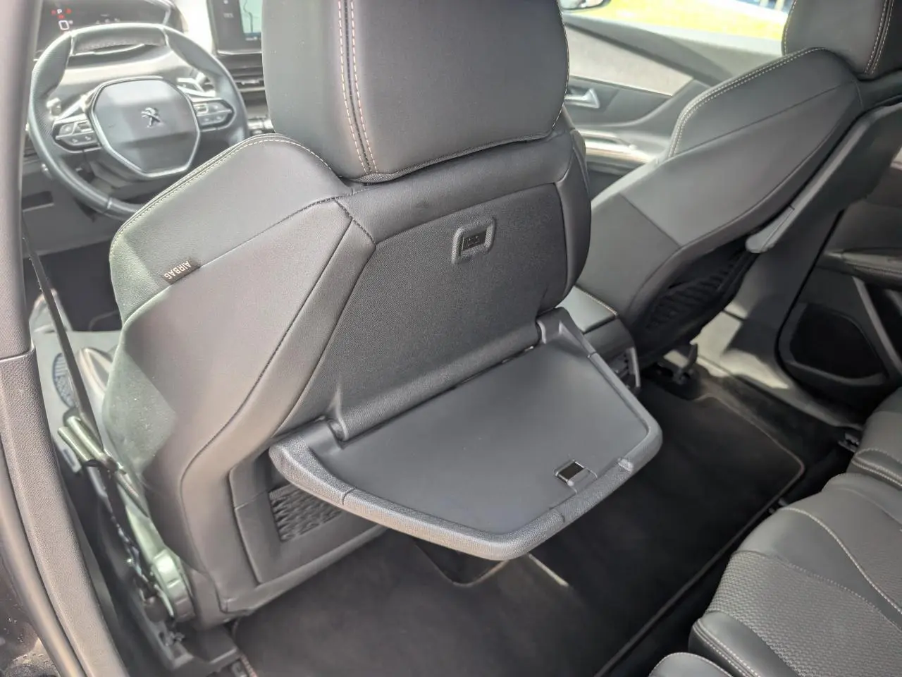 Vue intérieure arrière montrant le dossier du siège avant gauche gris avec tablette rabattable déployée sur un Peugeot 5008 GT 2023.