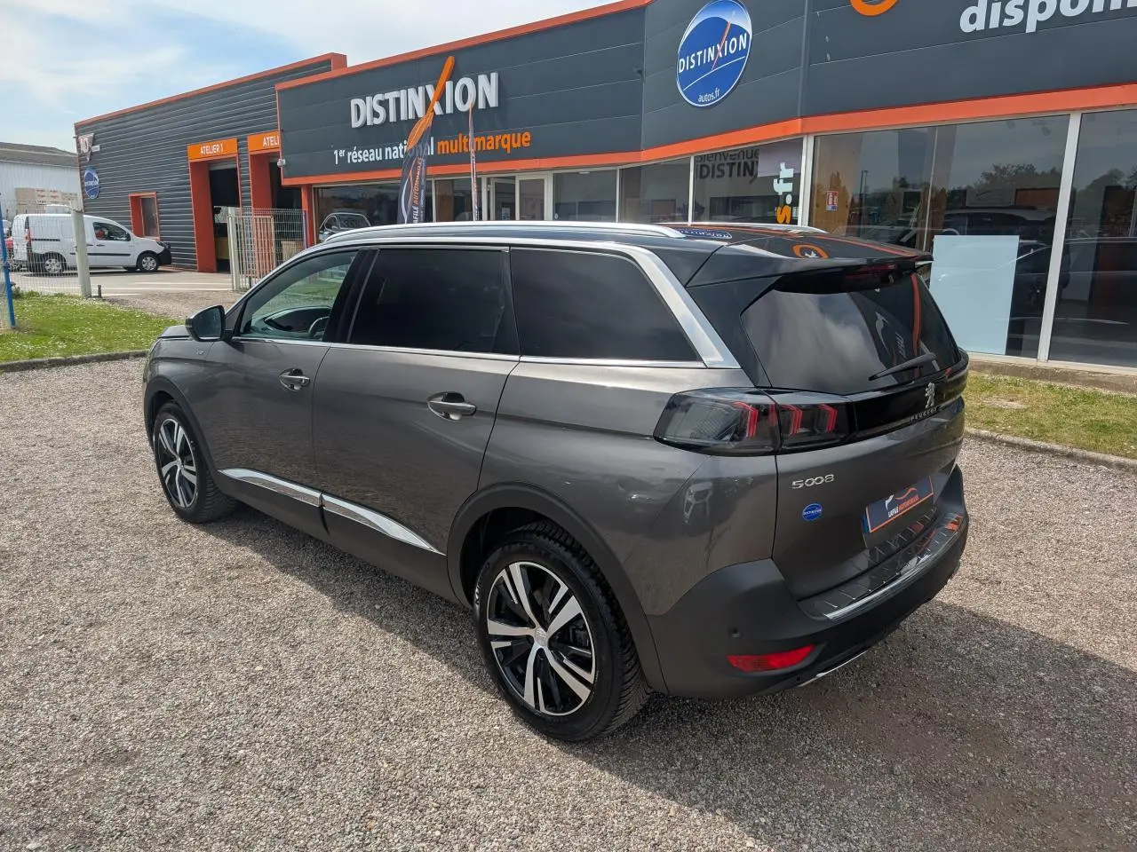 Vue 3/4 arrière droit d’un Peugeot 5008 gris métallisé avec jantes bi-ton et vitres arrière surteintées.