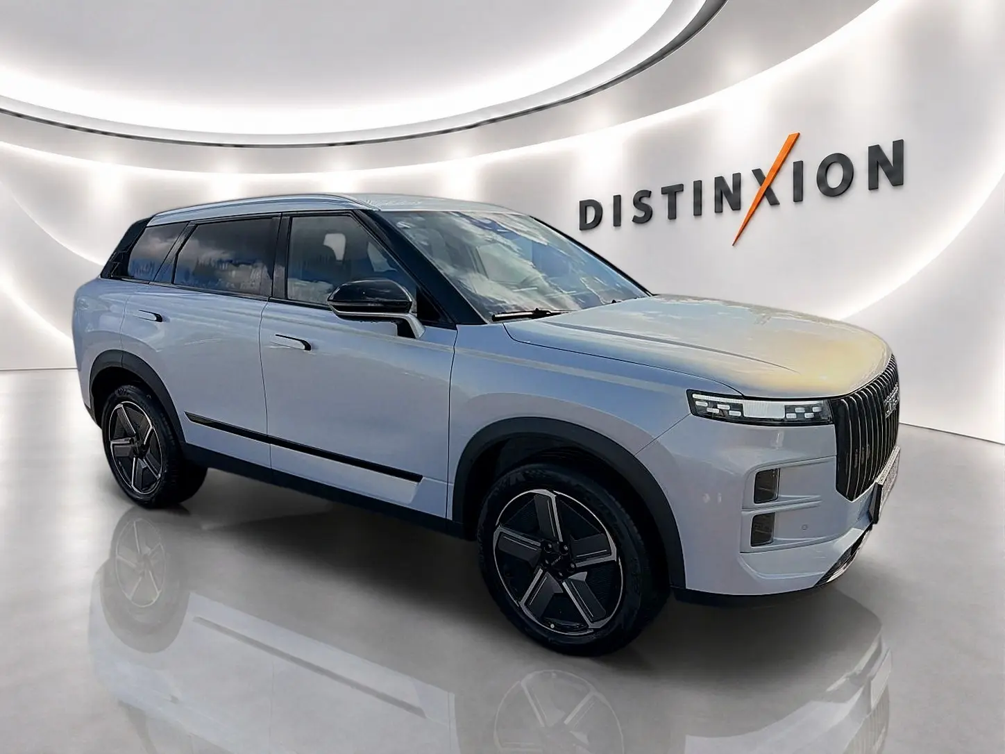 SUV JAECOO J7 gris moonlight vu en 3/4 avant droit dans un showroom lumineux avec jantes alu noires.