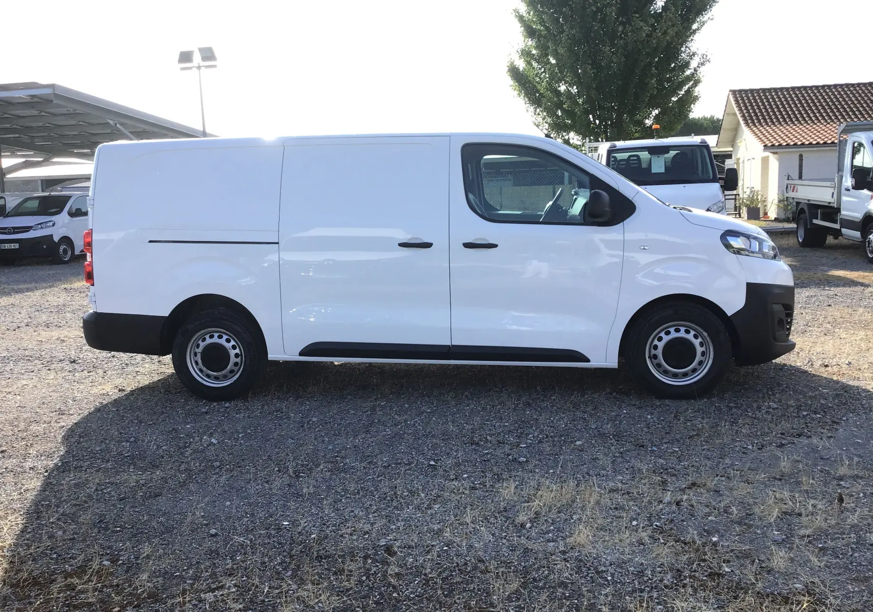 Profil droit d’un utilitaire blanc Citroën Jumpy XL 2.0 BlueHDi 120 Premium 3 places, stationné sur un sol gravillonné.