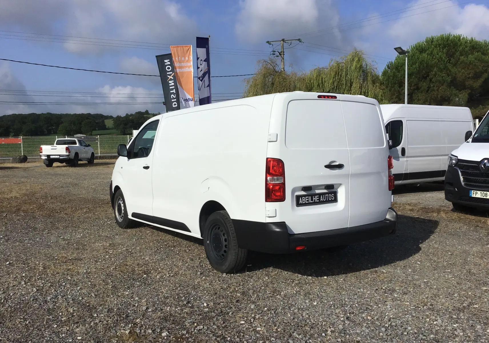Vue 3/4 arrière droite d'un utilitaire Citroën Jumpy XL blanc, avec portes arrière fermées sur un parking extérieur.