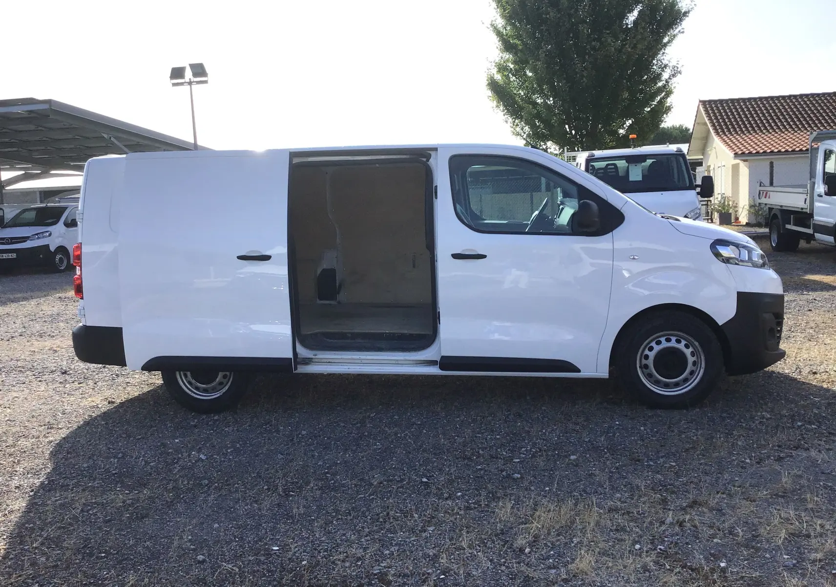 Vue latérale droite d'un utilitaire Citroën Jumpy XL blanc avec porte coulissante ouverte sur un parking extérieur.
